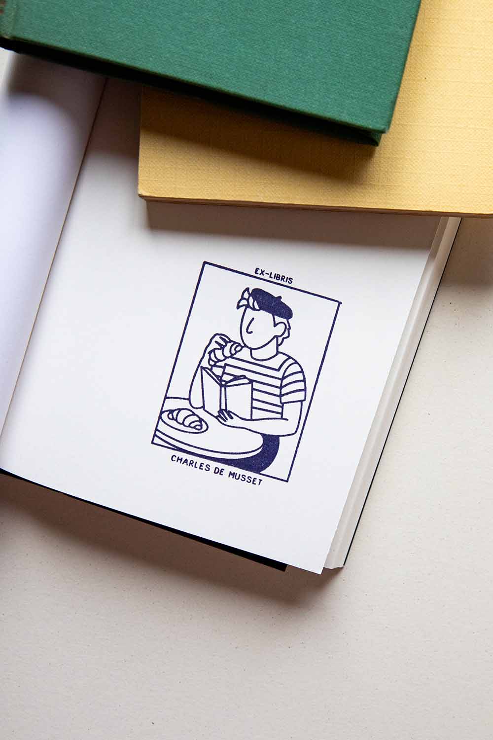 Portadilla de libro estampado con una persona comiendo croissants y leyendo un libro en una terraza de bar parisino