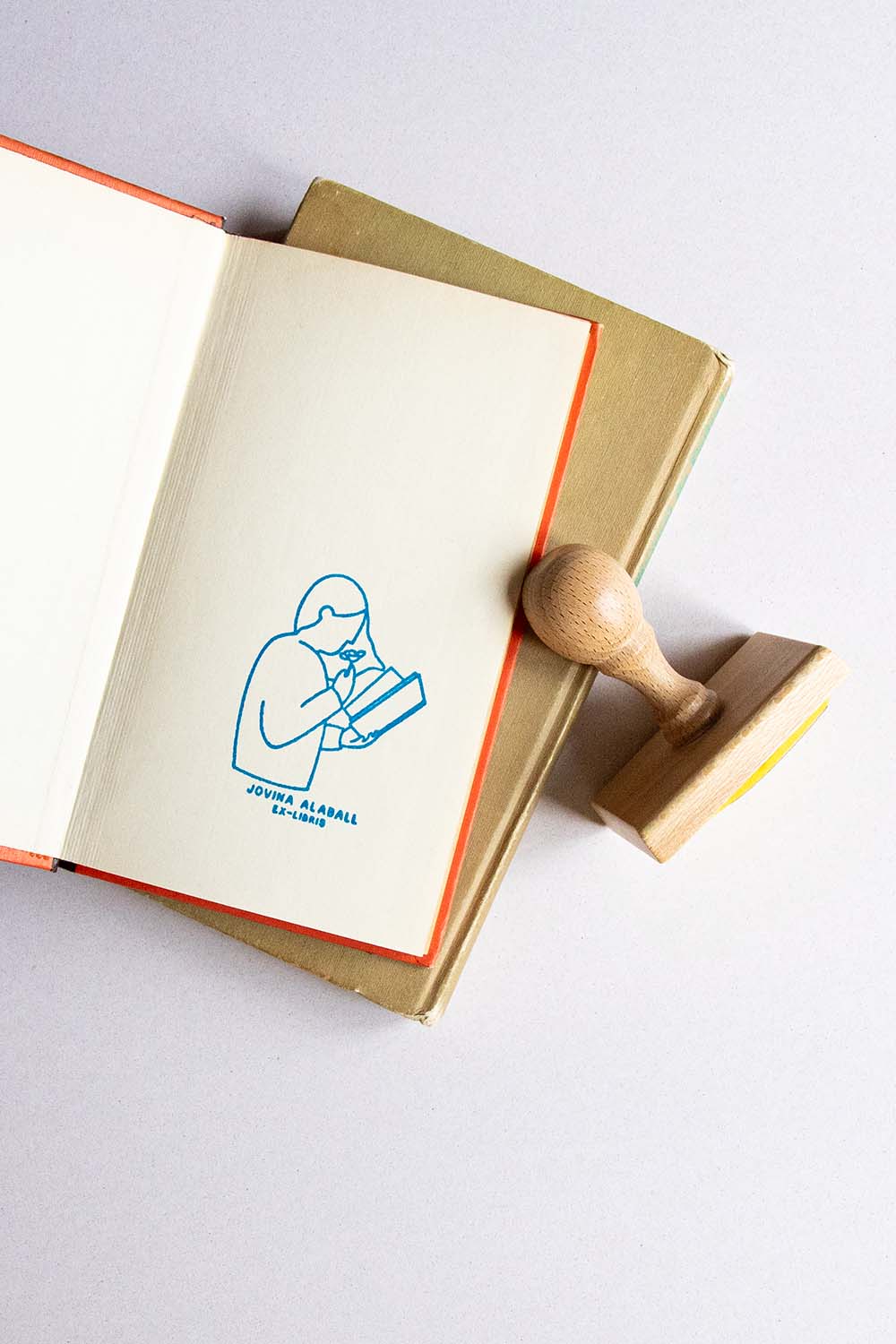Portadilla de libro estampada con una lectora leyendo y oliendo una rosa y sello