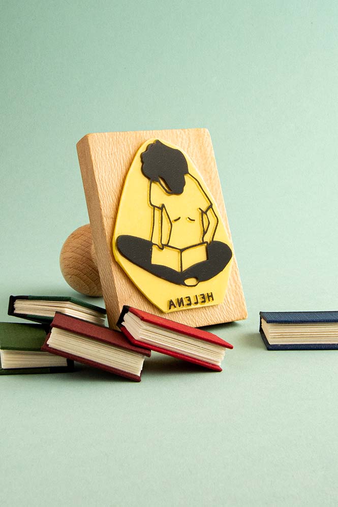 Sello exlibris grabado de una persona sentada con las piernas cruzadas leyendo un libro