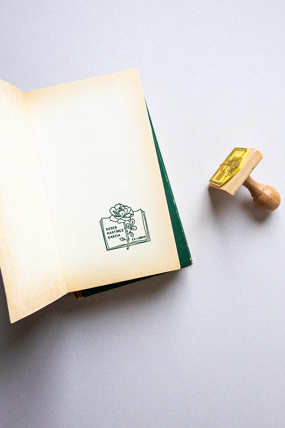 Portadilla de libro estampada con sello exlibris de un libro abierto con rosa encima y sello