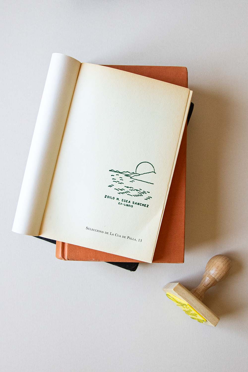 Portadilla de un libro estampada con un paisaje en pleno amanecer y sello