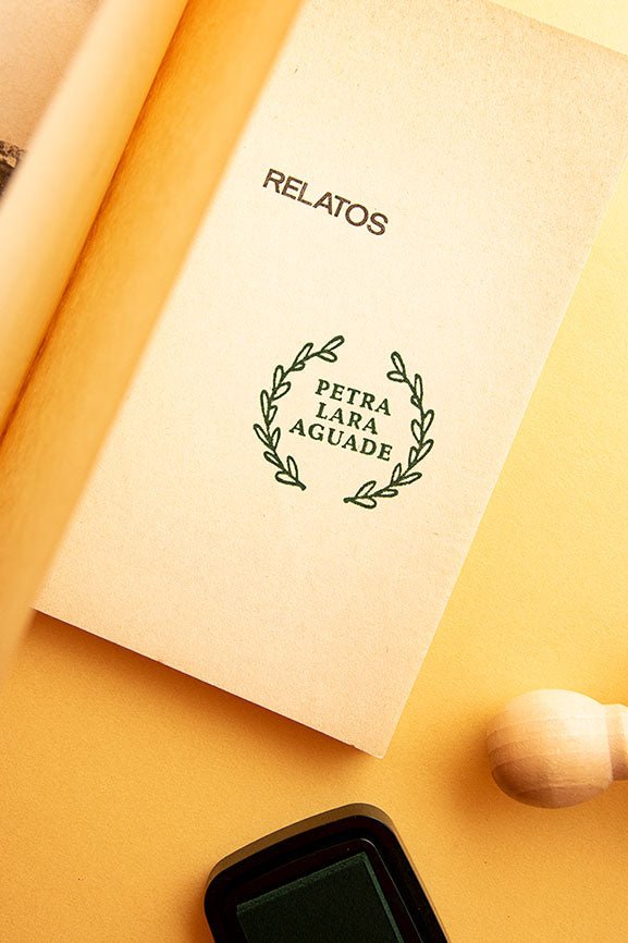 Portadilla de libro estampada con un sello exlibris de un círculo de hojas de laurel que enmarcan el nombe del propietario y sello