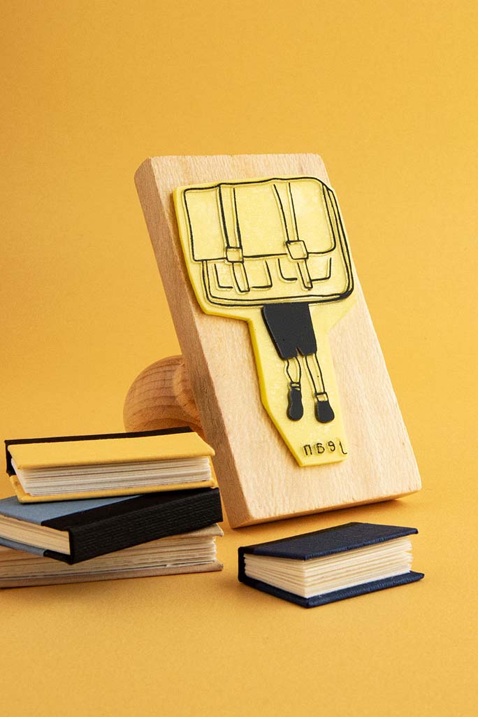 Sello exlibris grabado con un niño que lleva una mochila tan grande que solo vemos sus piernas y pies