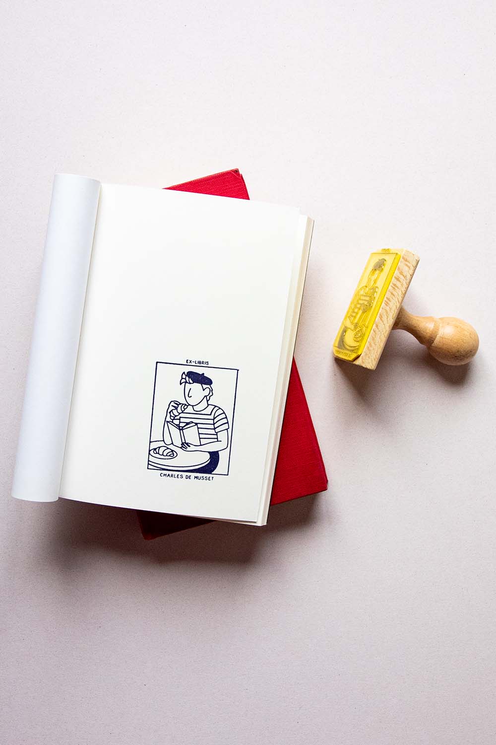 Portadilla de libro estampado con una persona comiendo croissants y leyendo un libro en una terraza de bar parisino y sello