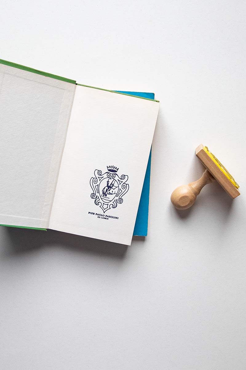 Portadilla de libro estampado con un escudo heráldico con una corona, dentro del escudo se ve una mano escribiendo con una pluma