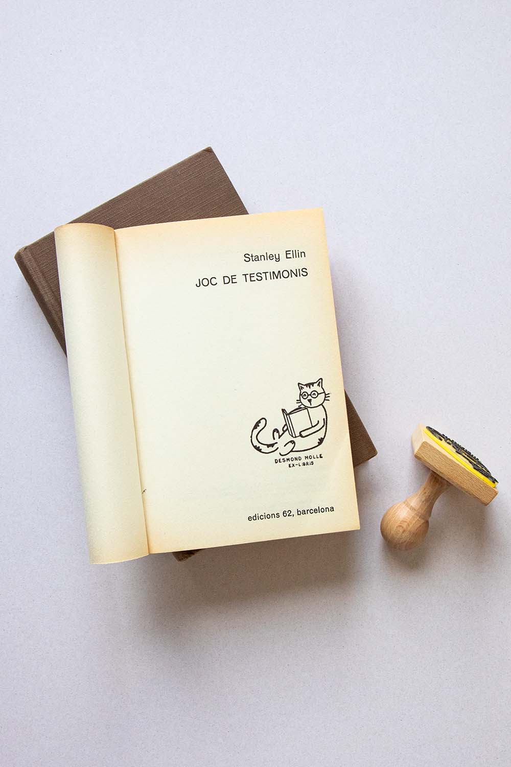 Portadilla de libro estampada con sello exlibris de un gato con gafas tumbado leyendo un libro y sello