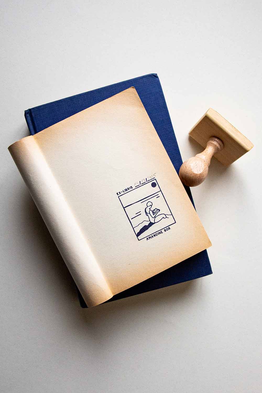 Portadilla de un libro estampada con una mujer leyendo junto al mar y sello