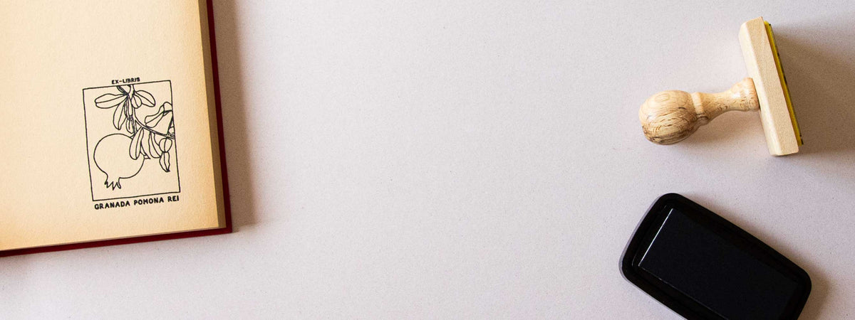 Exlibris personalizzato timbrato sulla pagina di guardia di un libro aperto, con un melograno