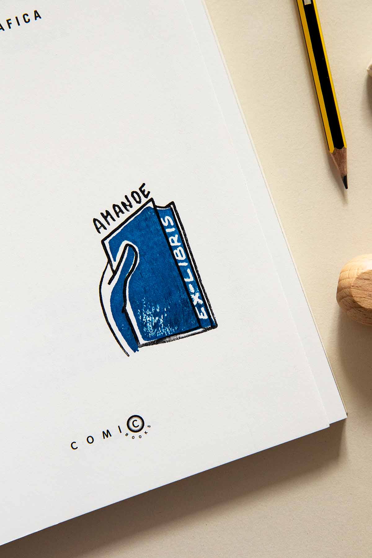 Portadilla de libro estampada con un sello exlibris de una mano cogiendo un libro azul