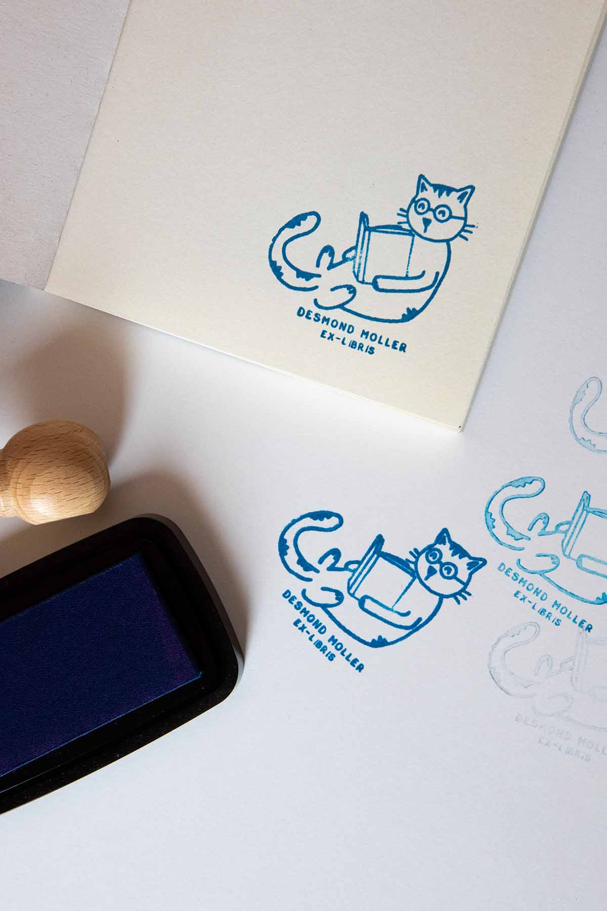 Portadilla de libro estampada con sello exlibris de un gato con gafas tumbado leyendo un libro